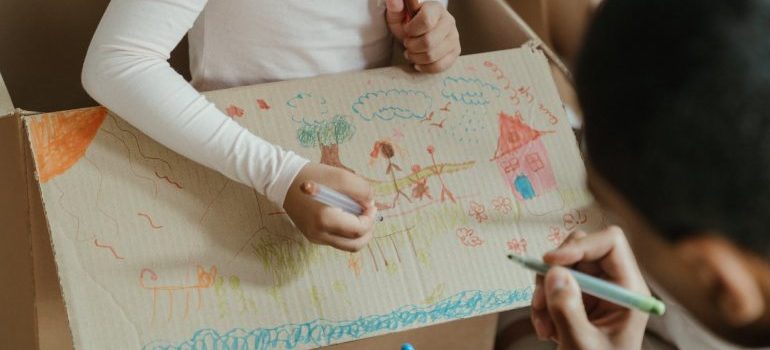 A father and daughter drawing on a moving box.