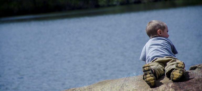 A kid laying on the bank of a lake