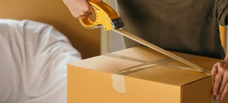 A man taping up a cardboard box before hiring the best movers in Westland MI.