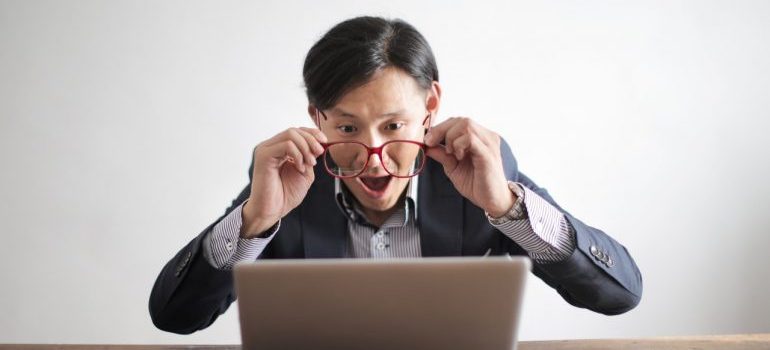 A surprised man holding his glasses and looking at his laptop that contains information about movers Brighton MI 